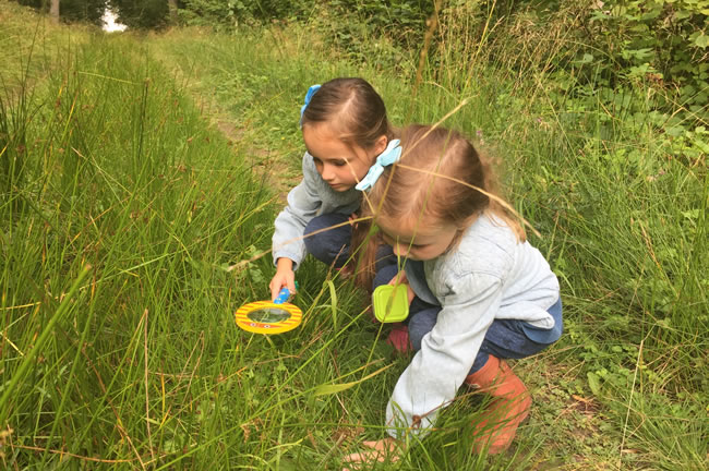 two children looking for mini beasts in grass