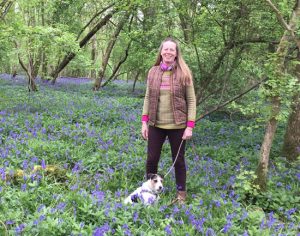 woman with a small dog standing in bluebells in a wood